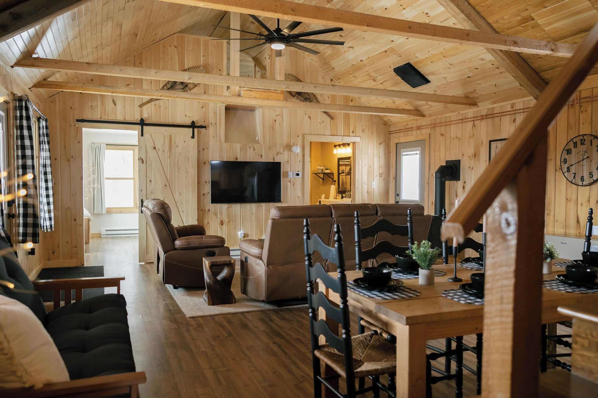 A wooden interior with a TV, leather sofas, a dining table, and a staircase.