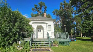Un piccolo edificio bianco con un portico verde, immerso nel verde e circondato da alberi.