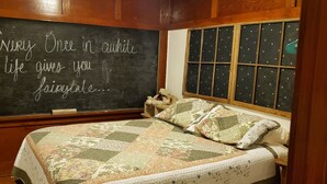 Una stanza accogliente con un letto, una coperta trapuntata, una finestra decorata con motivi a stella e una lavagna con una citazione.
