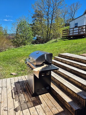 A barbecue grill on a wooden deck with a grassy yard and trees in the background.