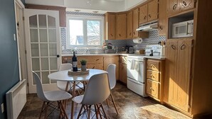 Una cocina moderna con armarios de madera, una mesa de comedor con sillas, un ventilador de techo y un ventanal que proporciona luz natural.