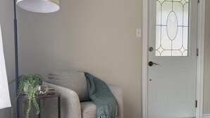 Una habitación con un sillón gris, un otoman redondo, una lámpara de pie y una planta en maceta.