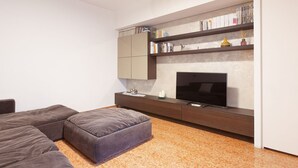 A modern living room with a sectional sofa, a flat-screen TV, a bookshelf, and a small table with a lamp. - GuestHost - Arco della Pace Apartment Milan (Milan)