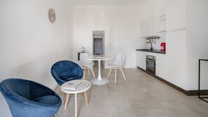 Een moderne keuken met witte kastjes, een rode koffiemachine, en een klein eethoekje met een ronde tafel en twee stoelen.