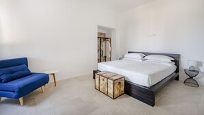 Een slaapkamer met een bed, een blauwe bank, een tafeltje en een opbergkist.