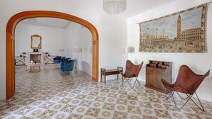 Une pièce avec des carreaux de sol à motifs, une arche en bois, un lustre, un tableau représentant un bâtiment historique et deux fauteuils en cuir.