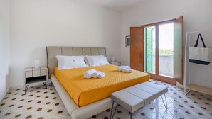 Une chambre à coucher avec un lit, un banc, une table de chevet, une fenêtre et une porte.