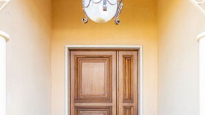 A wooden door with a simple design, a light fixture above it, and a plain wall. - GuestHost - Cozy detached villa of 156 sqm, on two levels, able to accommodate up to 9 people. The property is located in Pizzolungo, a coastal hamlet of Erice, an oasis of peace overlooking the crystalline sea of ​​​​western Sicily. A few minute (Pizzolungo)
