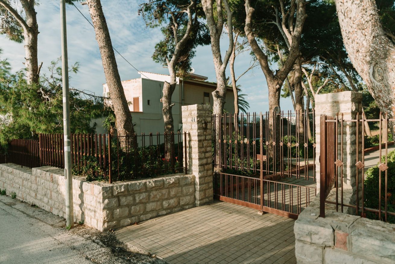 A gated residential area with stone walls, a paved entrance, and trees.