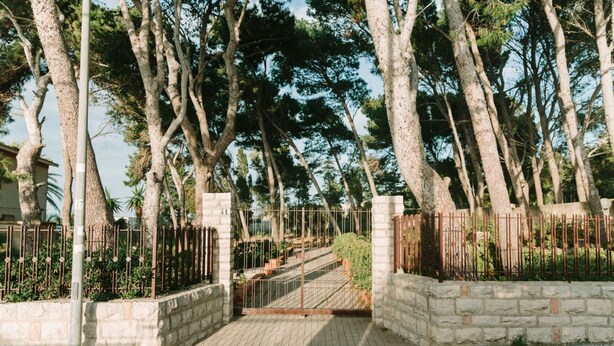 A gated entrance with a stone wall, metal gate, and a paved path leading through a wooded area. - GuestHost - Cozy detached villa of 156 sqm, on two levels, able to accommodate up to 9 people. The property is located in Pizzolungo, a coastal hamlet of Erice, an oasis of peace overlooking the crystalline sea of ​​​​western Sicily. A few minute (Pizzolungo)