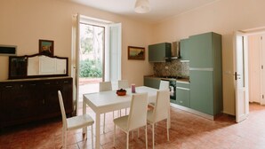 A dining area with a table and chairs, a kitchen with green cabinets, and a door leading outside. - GuestHost - Cozy detached villa of 156 sqm, on two levels, able to accommodate up to 9 people. The property is located in Pizzolungo, a coastal hamlet of Erice, an oasis of peace overlooking the crystalline sea of ​​​​western Sicily. A few minute (Pizzolungo)