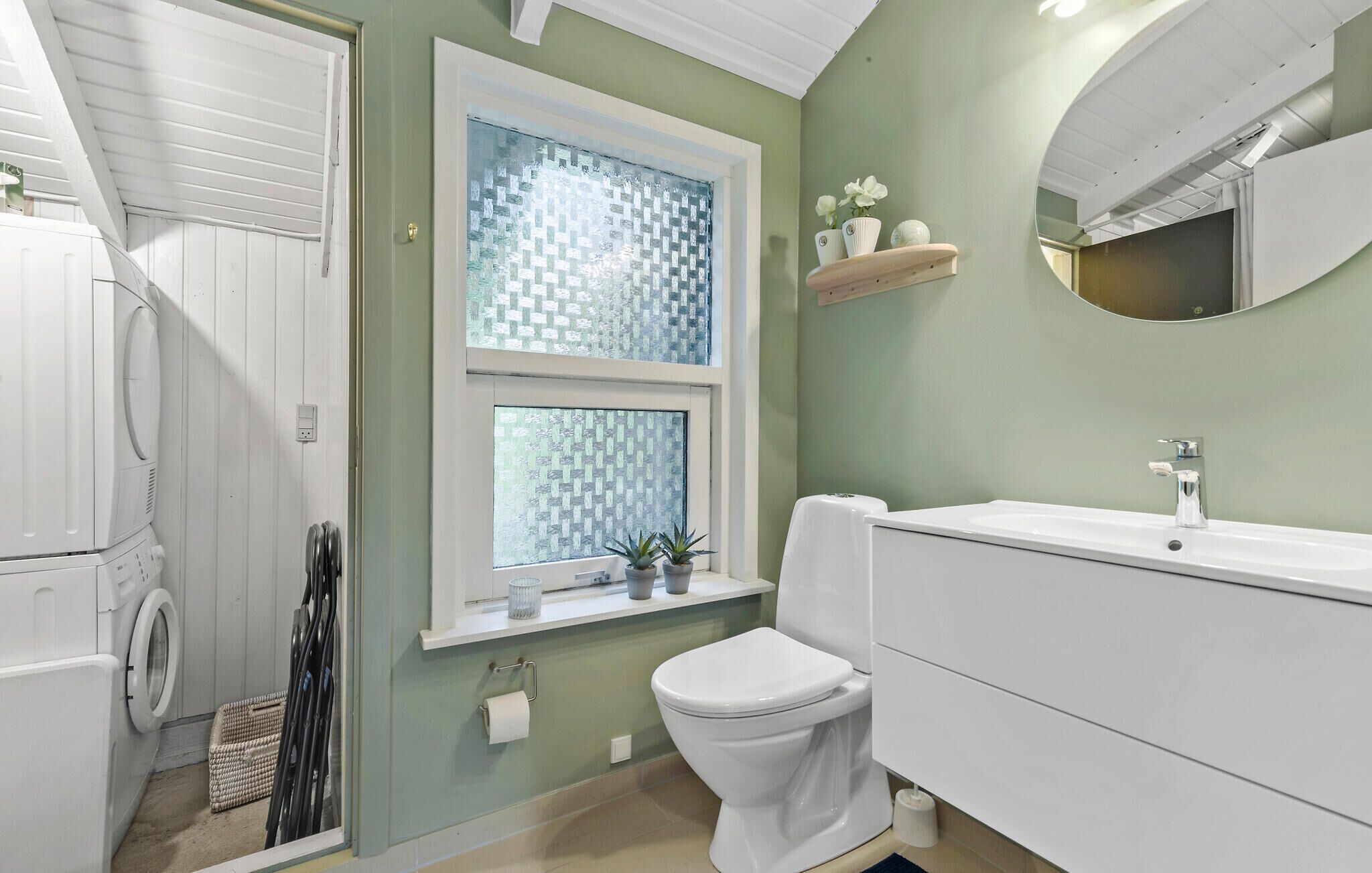 A bathroom with a white toilet, a sink with a mirror, a window with patterned glass, and a washing machine.