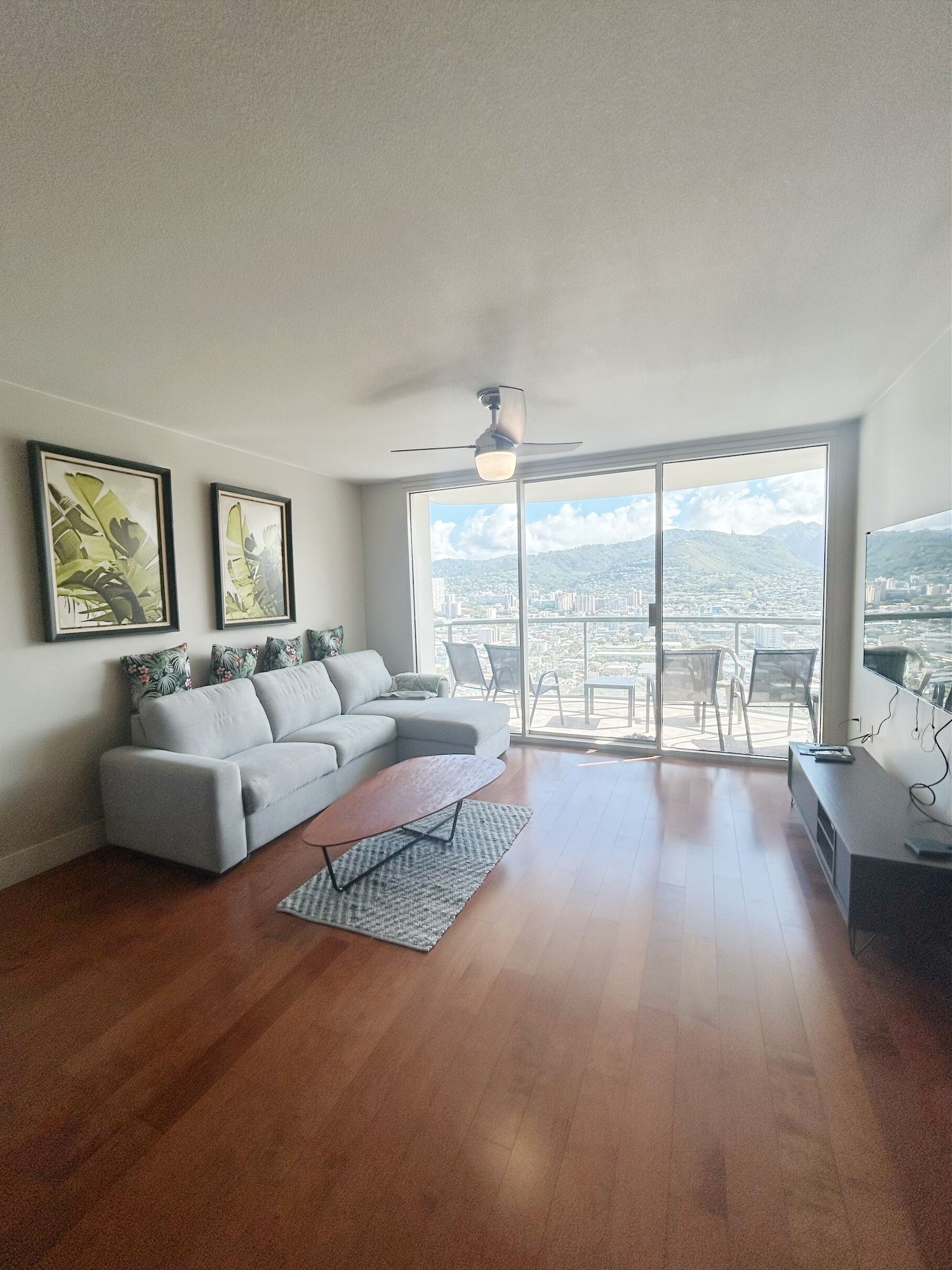 Ein geräumiges Wohnzimmer mit grauem Sofa, einem Couchtisch und einer großen Glasschiebetür, die auf einen Balkon im Freien führt.