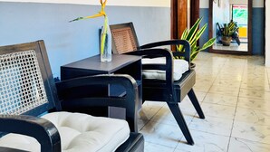 A hotel lobby with a seating area featuring two black chairs with white cushions, a small table with a bottle and a decorative item, and two framed paintings on the wall. - Tropical Mid-Century Modern B&B in Merida's Centro, Azul (Mérida)