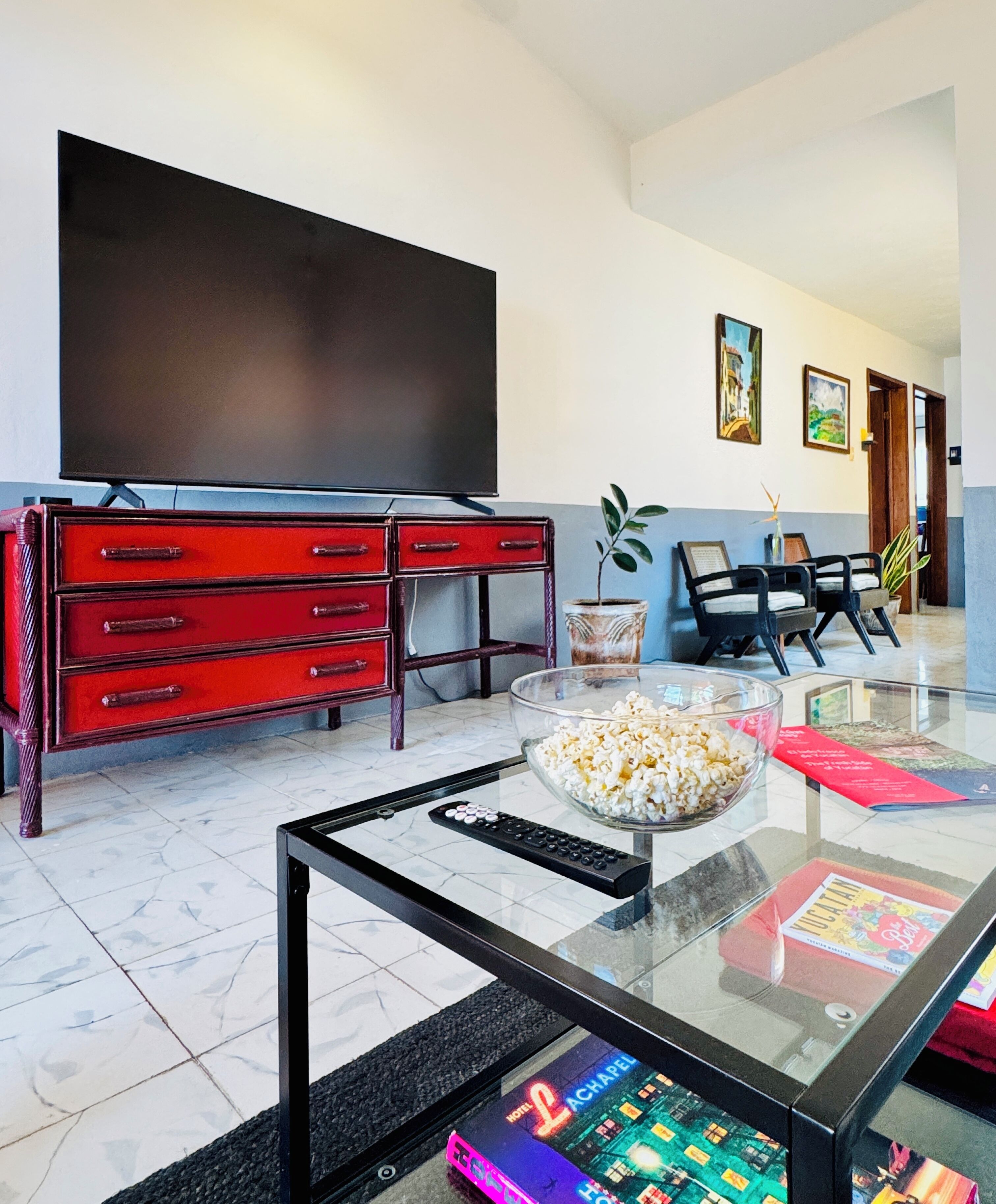 A modern living room with a glass coffee table, red entertainment unit, and a flat-screen TV.