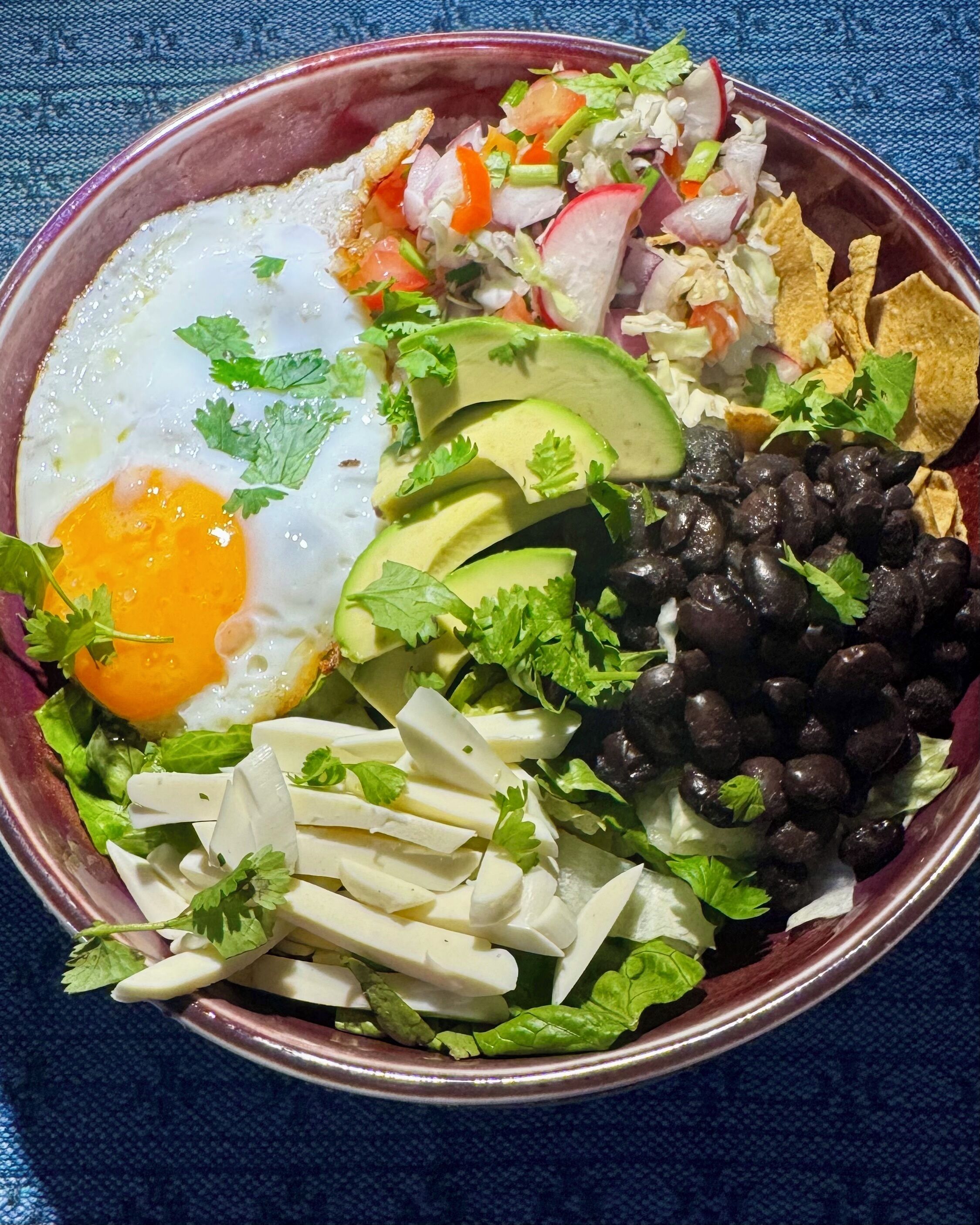 En skål mad med spejlæg, avocado, sorte bønner og forskellige grøntsager.