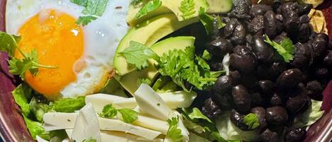 En skål mad med spejlæg, avocado, sorte bønner og forskellige grøntsager.