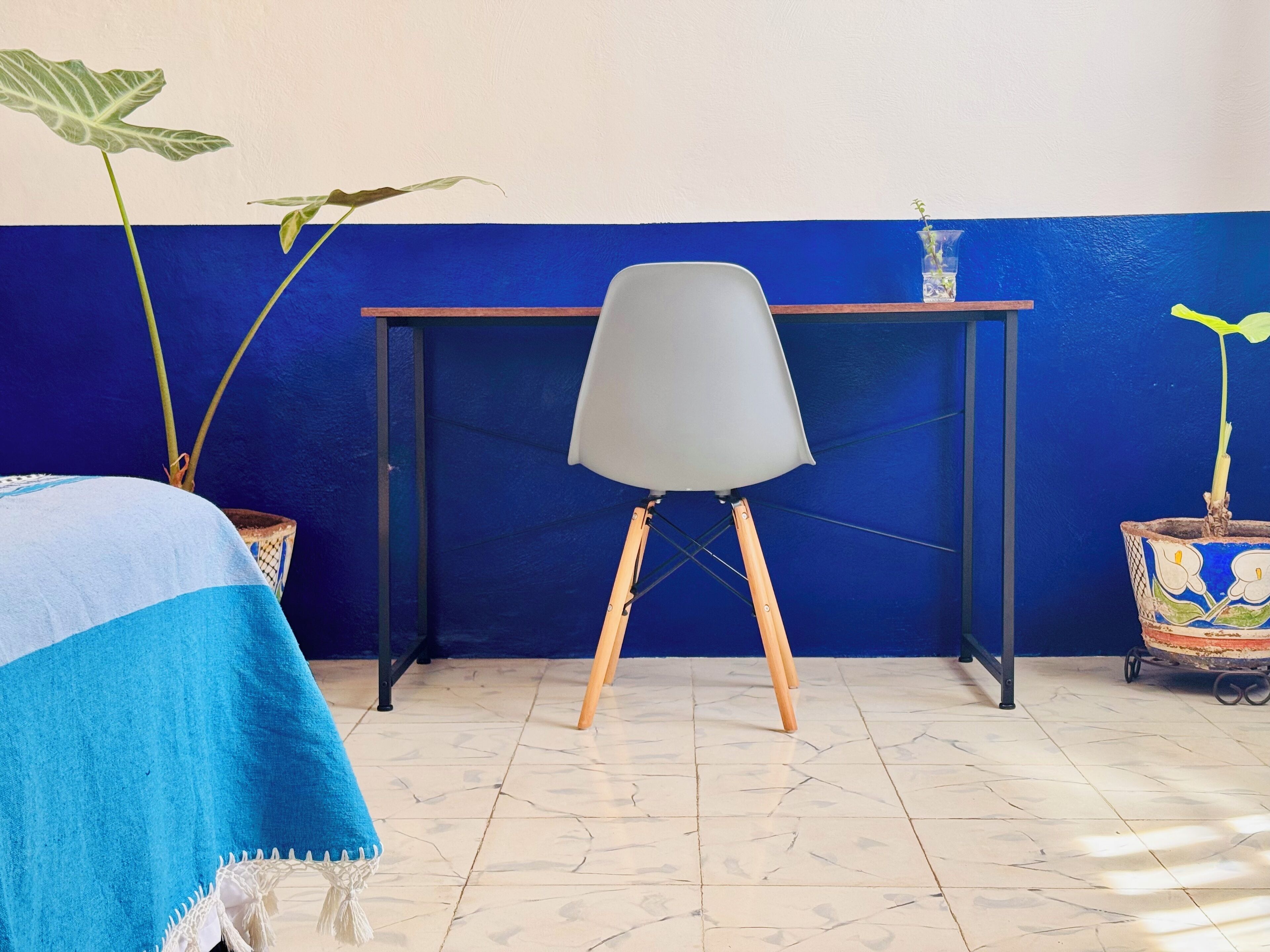 A room with a bed, a desk, and two potted plants.