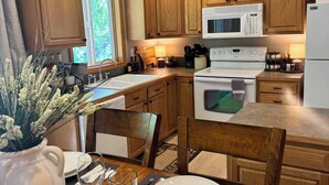 Une cuisine moderne avec des meubles en bois, un four à micro-ondes blanc et une cuisinière. On y trouve une table à manger mise avec des assiettes, des verres et un vase de fleurs.
