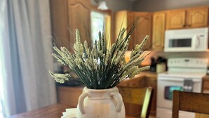 Un vase en céramique blanche, doté de deux anses, est posé sur une table en bois dans une cuisine dont les meubles et le four à micro-ondes sont également en bois.