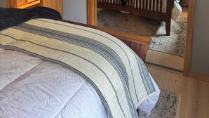 Une chambre avec un grand lit, une table de chevet avec une lampe et une tête de lit en bois. Il y a une porte qui donne sur une autre pièce et un miroir sur le mur.