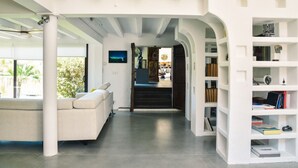 A modern interior with a white sofa, a bookshelf, and a staircase leading to another room. - Les Nymphéas, Landes haven of peace, nature & private pond (Angresse)