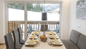 A dining area with a long table set for six, a sofa, and a view of a snowy landscape through large windows. - Nice apartment for 5 people with WIFI, TV and balcony (Wildschönau)
