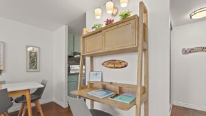A dining area with a white table and chairs, a wooden desk with a laptop, and a wall-mounted shelf with decorative items. - Legal Studio with AC and WiFi, Just One Block from Waikiki Beach (Honolulu)
