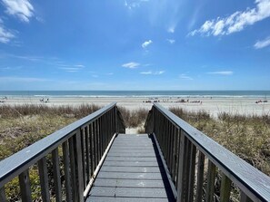 A wooden boardwalk leading to a beach with a clear sky.
