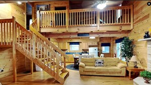 A cabin interior with a wooden staircase, a dining area, a sofa, and a plant.