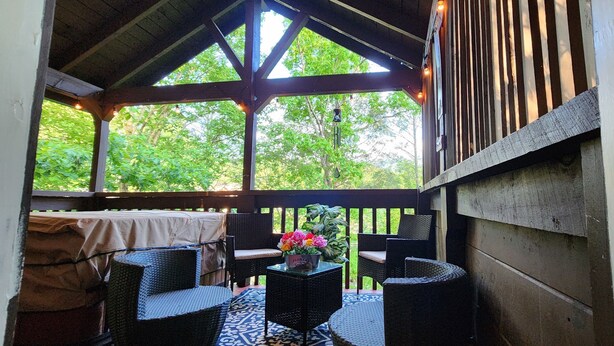 An outdoor patio with wicker furniture, a table with flowers, and a view of greenery.