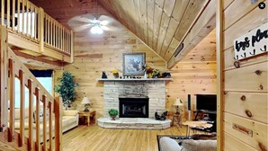 A wooden interior with a fireplace, a sofa, a dining table, and a staircase.