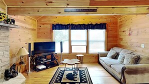 A cozy cabin interior with a wooden interior, a sofa, a TV, a fireplace, and a window with curtains.