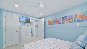 Een slaapkamer met een bed, een dressoir, een plafondventilator en kunst aan de muur.