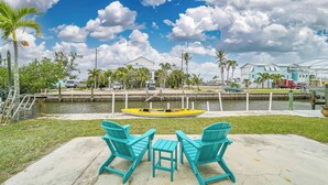 Uitzicht op het water met een aangemeerde kajak, turquoise stoelen en een kleine tafel.