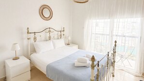 Un dormitorio con cama, mesitas de noche, lámpara colgante, ventana con cortinas y vistas al exterior.