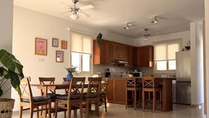 Una cocina moderna con armarios de madera, una isla central y un comedor con sillas de madera.