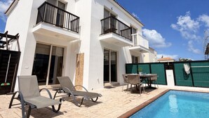 Una casa de dos pisos con piscina, mobiliario exterior y cerca verde.