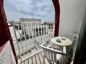 A balcony with a white railing, a small table with two chairs, and a view of a building with a white facade. - STAY NISSI Chrysland Studio 215 (Ayia Napa)