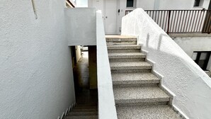 Un escalier étroit menant à une porte blanche, bordé de murs blancs et d’une rambarde en métal.