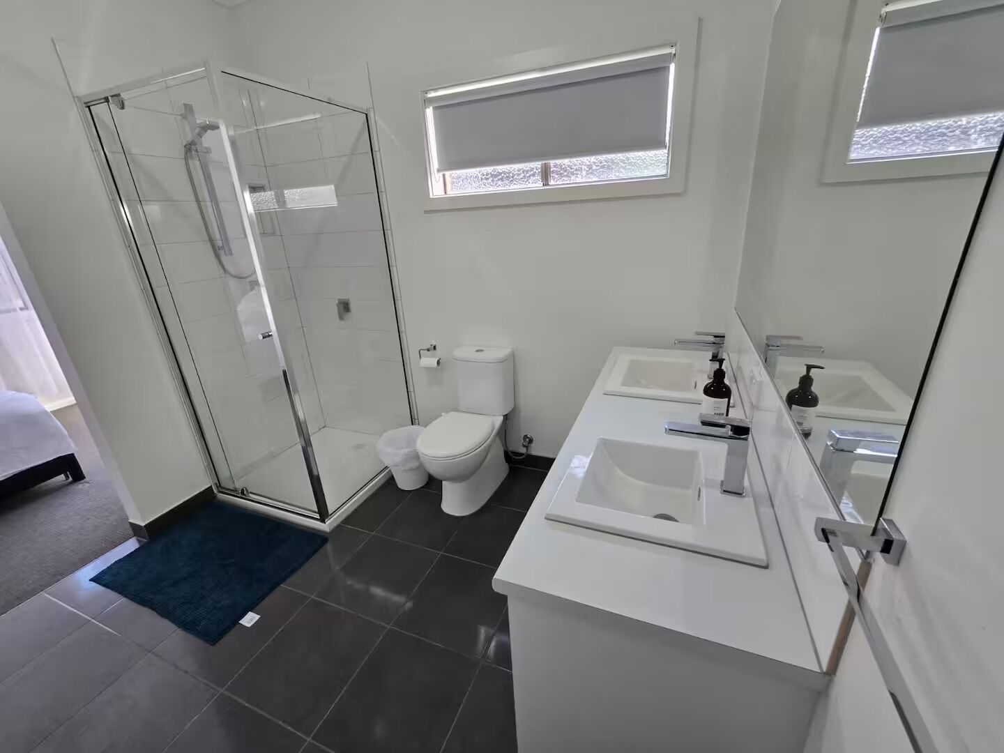 A modern bathroom with a glass shower enclosure, a toilet, and a double sink vanity.