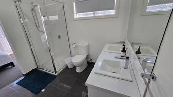 A modern bathroom with a glass shower enclosure, a toilet, and a double sink vanity.