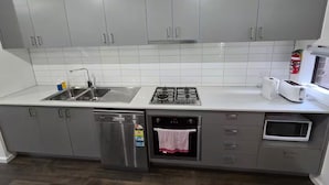 A modern kitchen with grey cabinets, a stainless steel sink, a gas stove, a dishwasher, a microwave, and a toaster. -  Serenity Home 7 by Hiverooms (Pakenham)