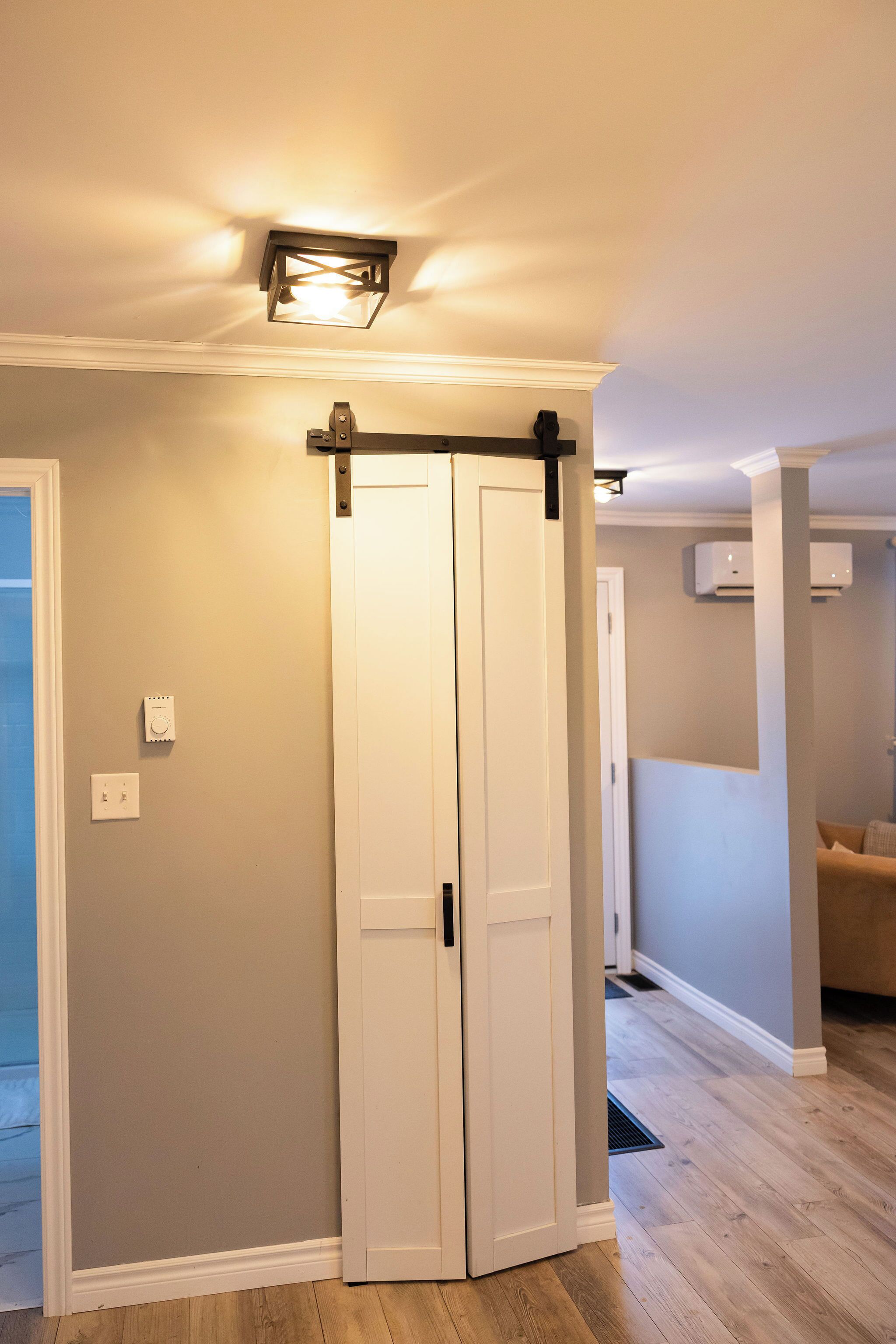 Un couloir avec une porte blanche, un luminaire et un appareil de climatisation.