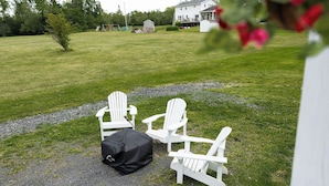 Twee witte Adirondack-stoelen, een zwarte tas en een grindpad in een gazon met een huis op de achtergrond.