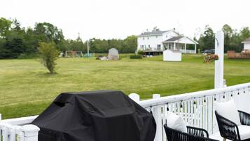 A covered grill on a deck with chairs and a view of a white house in the background.