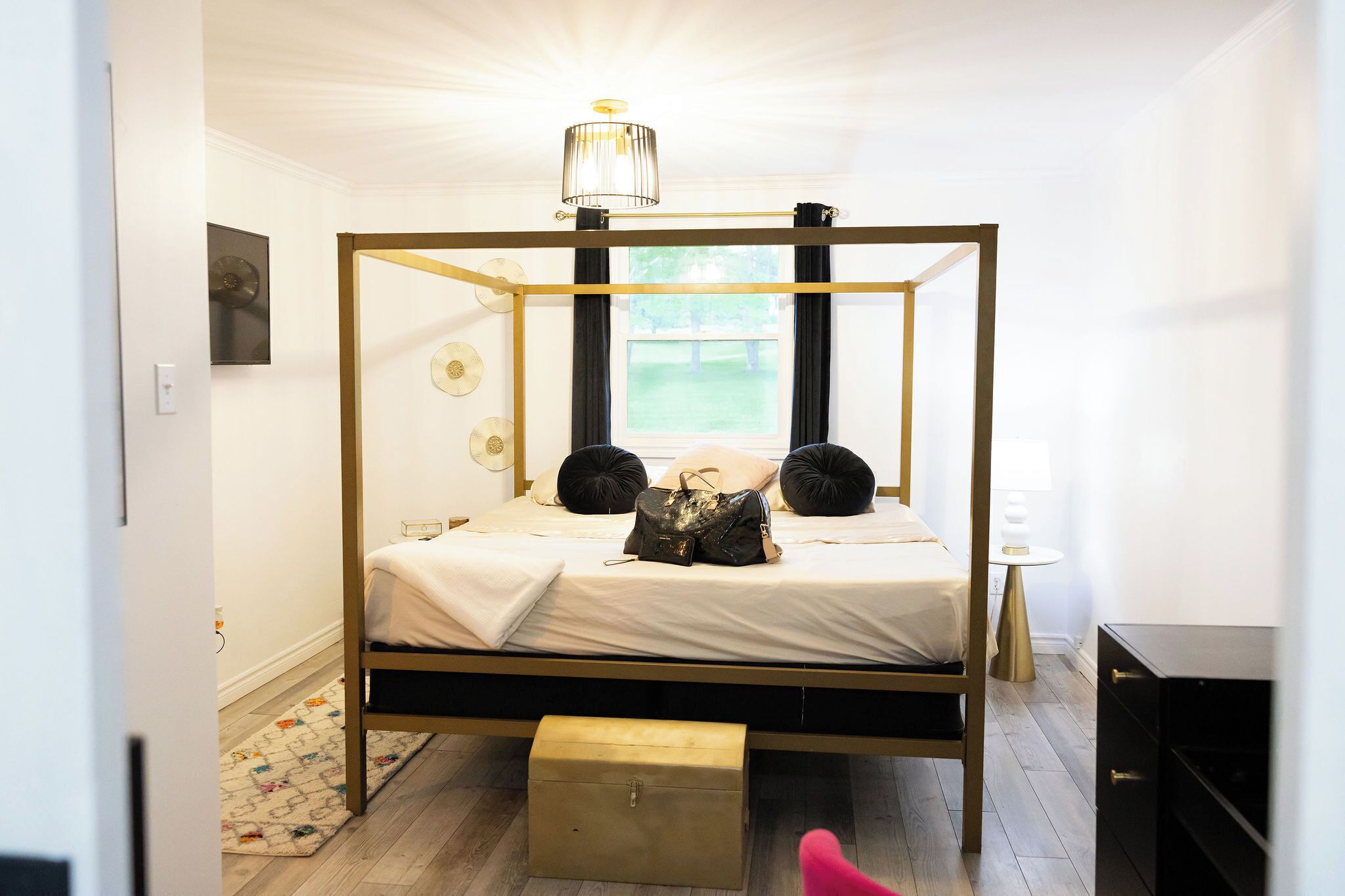 Un lit à baldaquin avec un cadre doré, une table de chevet, une lampe et une vue sur l’extérieur par une fenêtre.