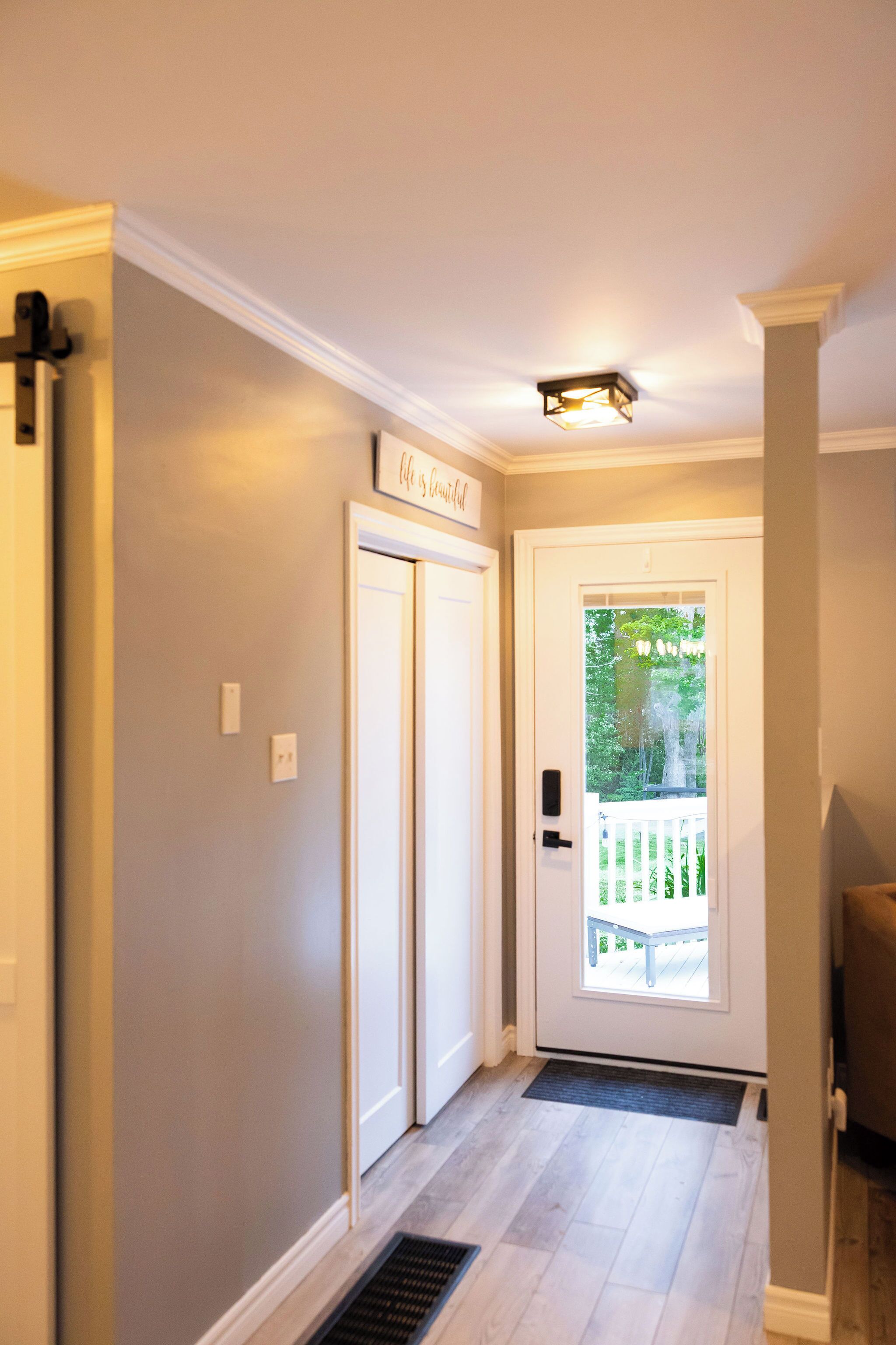 Un couloir avec une porte donnant sur un balcon, un luminaire au-dessus de la porte et une enseigne au-dessus de la porte.