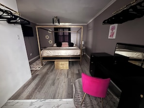 A bedroom with a bed, bedside table, lamp, dresser, and a mirror.