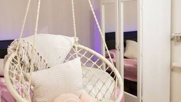 Une pièce avec un fauteuil suspendu en macramé, une armoire et un lit avec une literie rose.